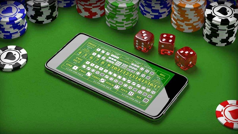 Phone showing a sic bo betting layout beside red dice and casino chips on a green felt table